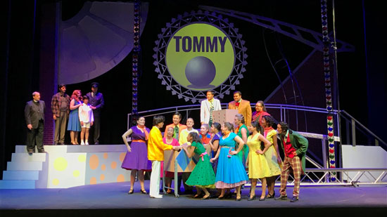 Several actors on stage in colorful costumes performing Tommy