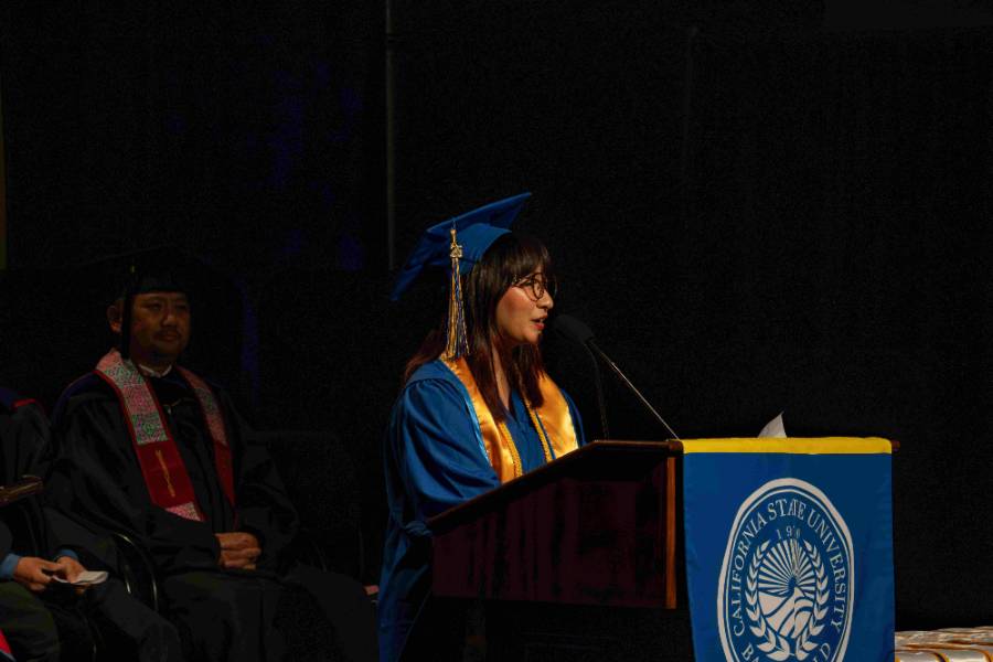 Asian American Pacific Islander Desi American (APIDA) Graduation Spring 2025 - Graduating student speaker, Deanne Manalastas, speaks at a wooden podium with a CSUB logo banner in front