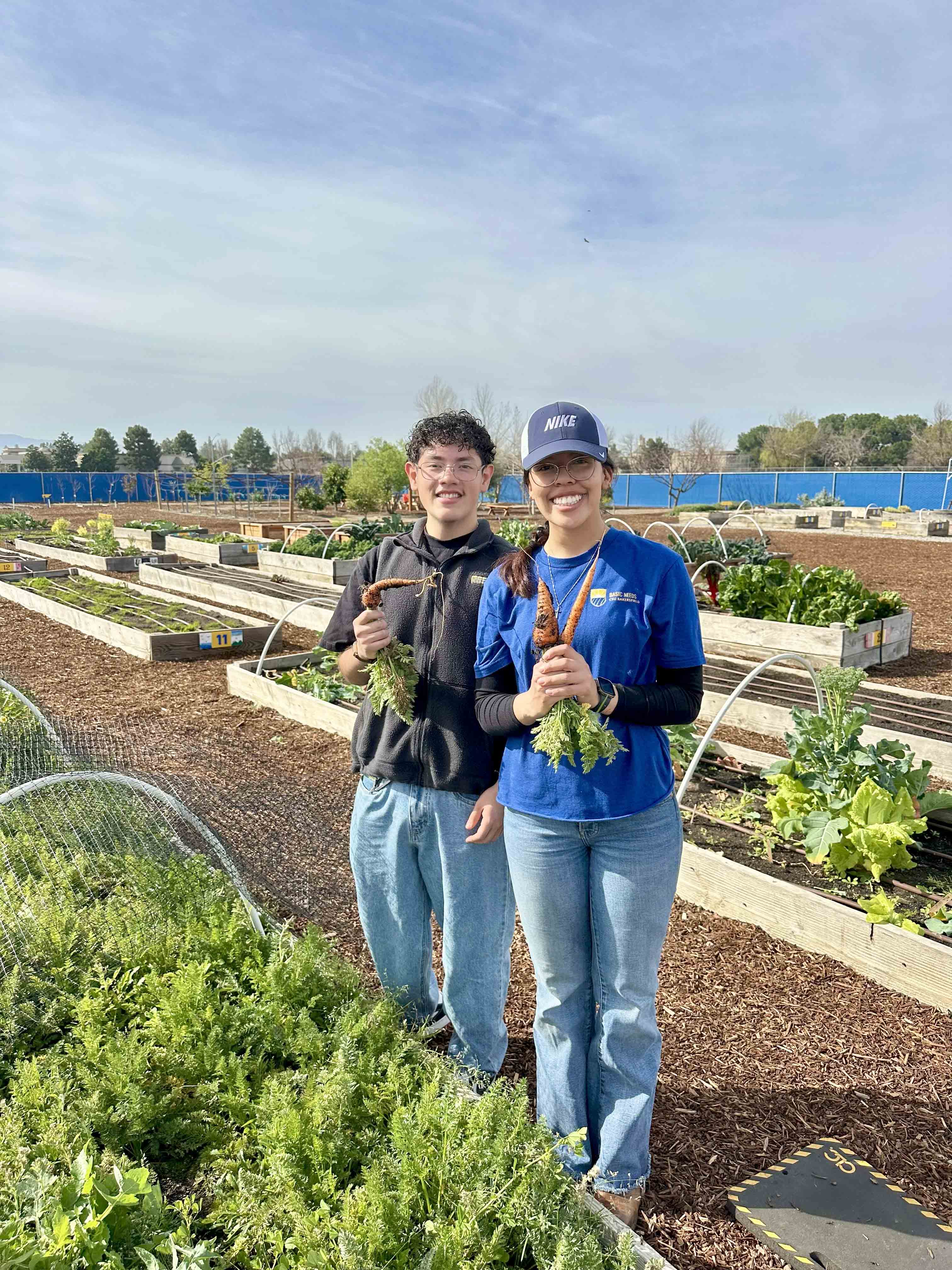 Two students holding carrots while standing amongst a sea of raised garden beds